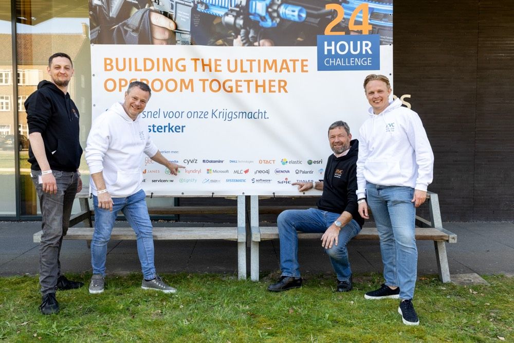 Four men stand before a poster reading "Building the ultimate Opsroom together"